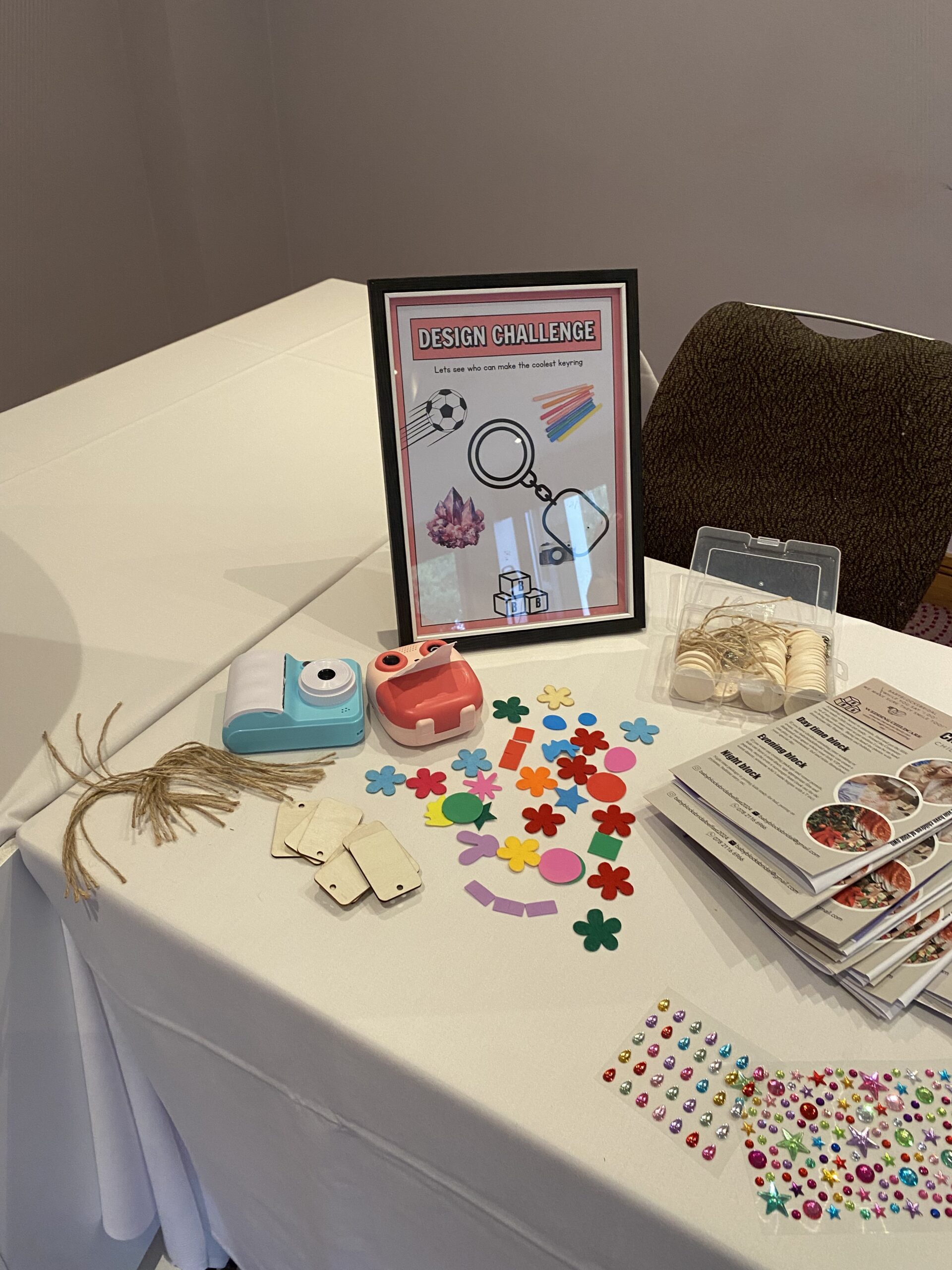 Craft table with design challenge sign, colorful foam shapes, string, and crafting tools on a white tablecloth.