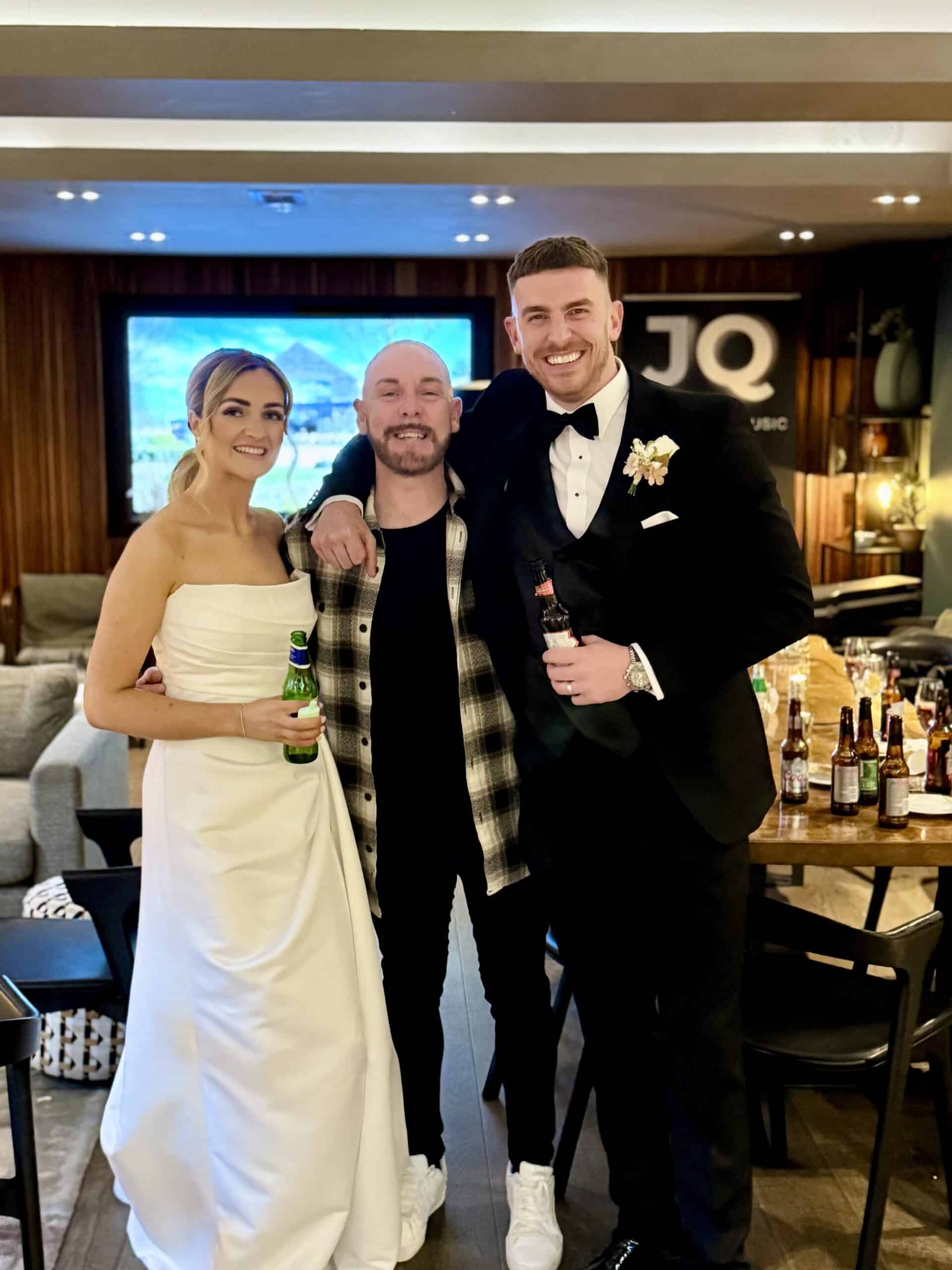 Three people smiling and posing together at a formal event, with one person in a wedding dress and another in a tuxedo.