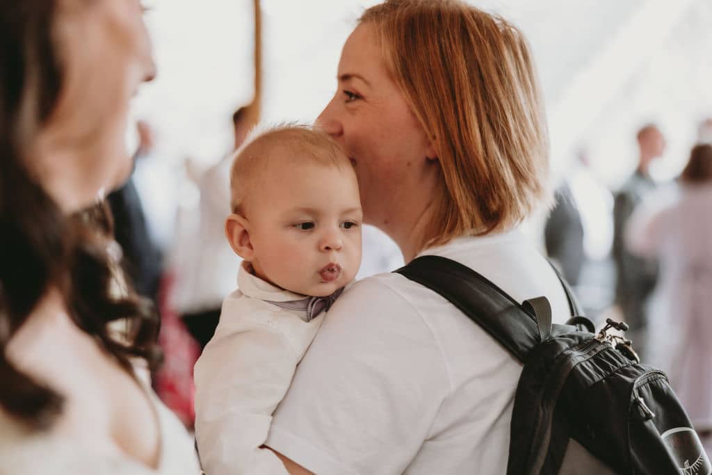 Woman holding a baby, surrounded by people in a softly lit indoor setting.