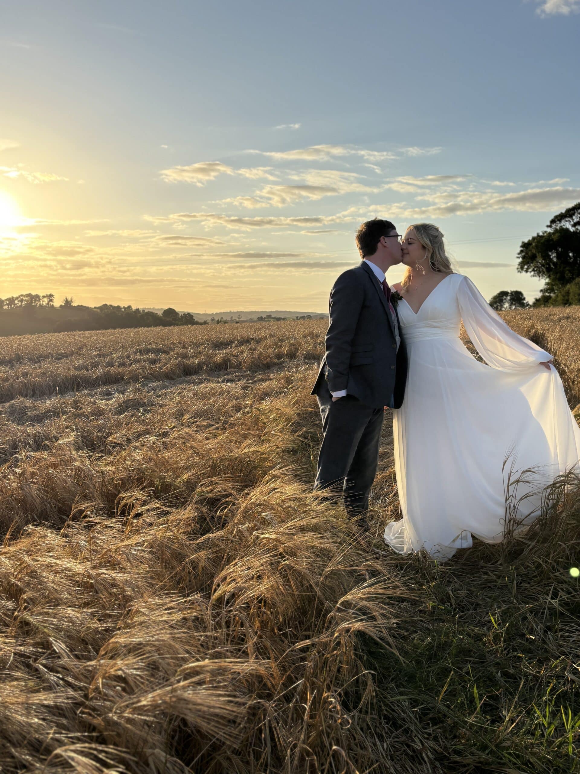 Bride and groom kissing in a sunlit field at sunset.