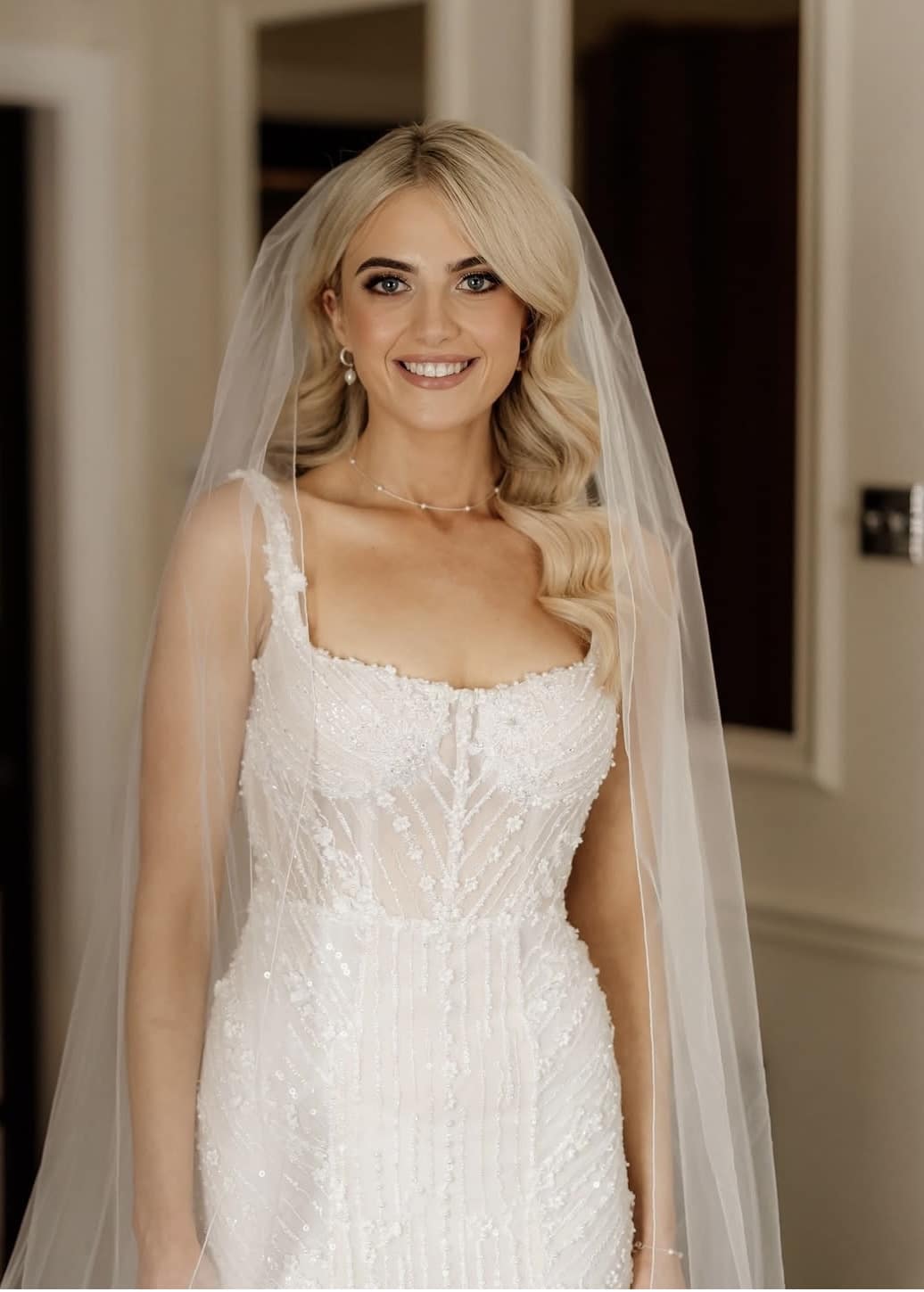 Bride in an elegant white wedding dress and veil, smiling.