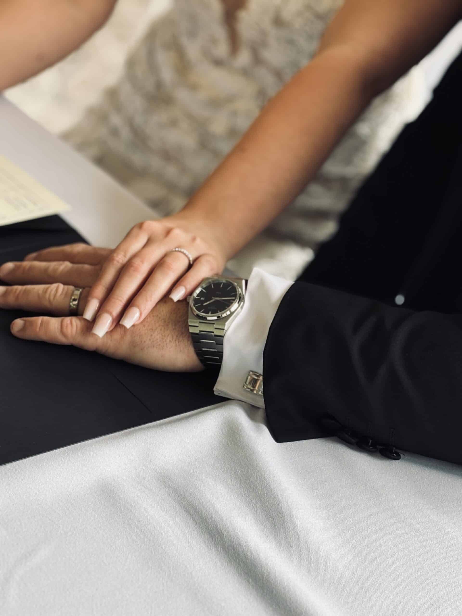 Bride and groom holding hands, showcasing wedding rings and a watch.