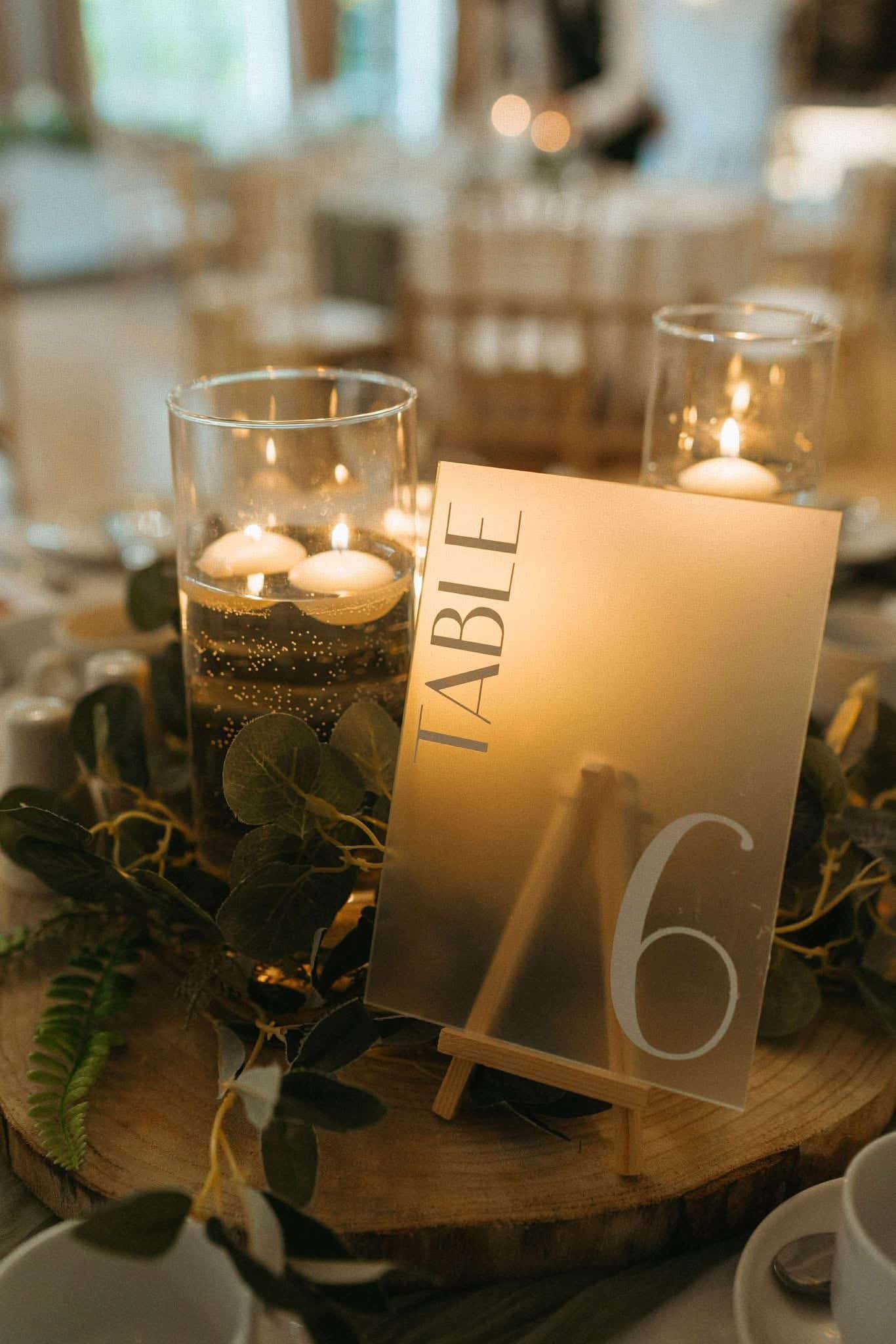Table 6 sign with floating candles and greenery on a wooden centerpiece.