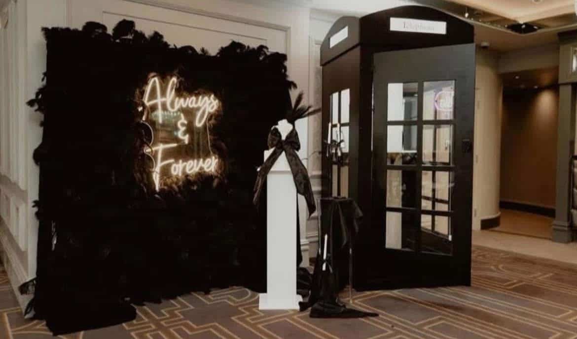 Neon "Always & Forever" sign with black decor and vintage phone booth in elegant setting.