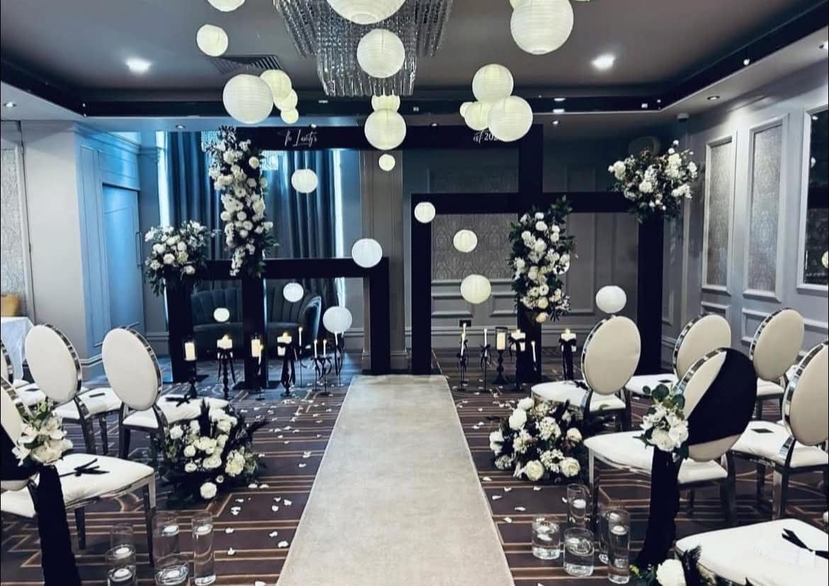 Elegant indoor wedding ceremony setup with white chairs, floral arrangements, candles, and hanging lanterns.