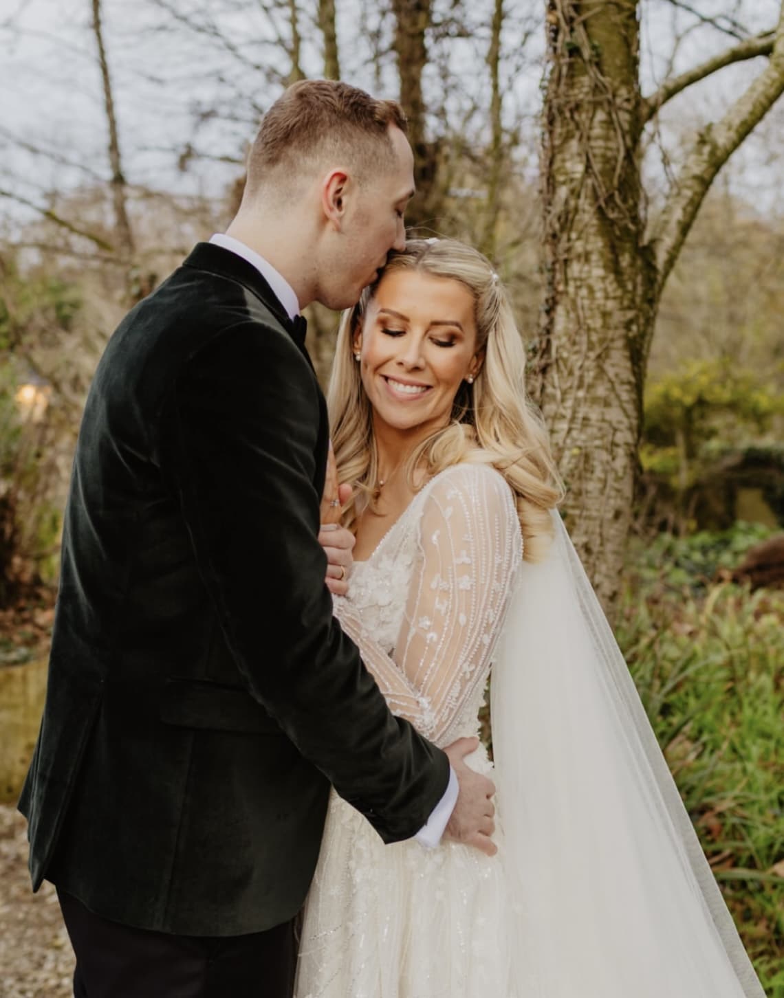 Bride and groom embracing in a wooded setting.