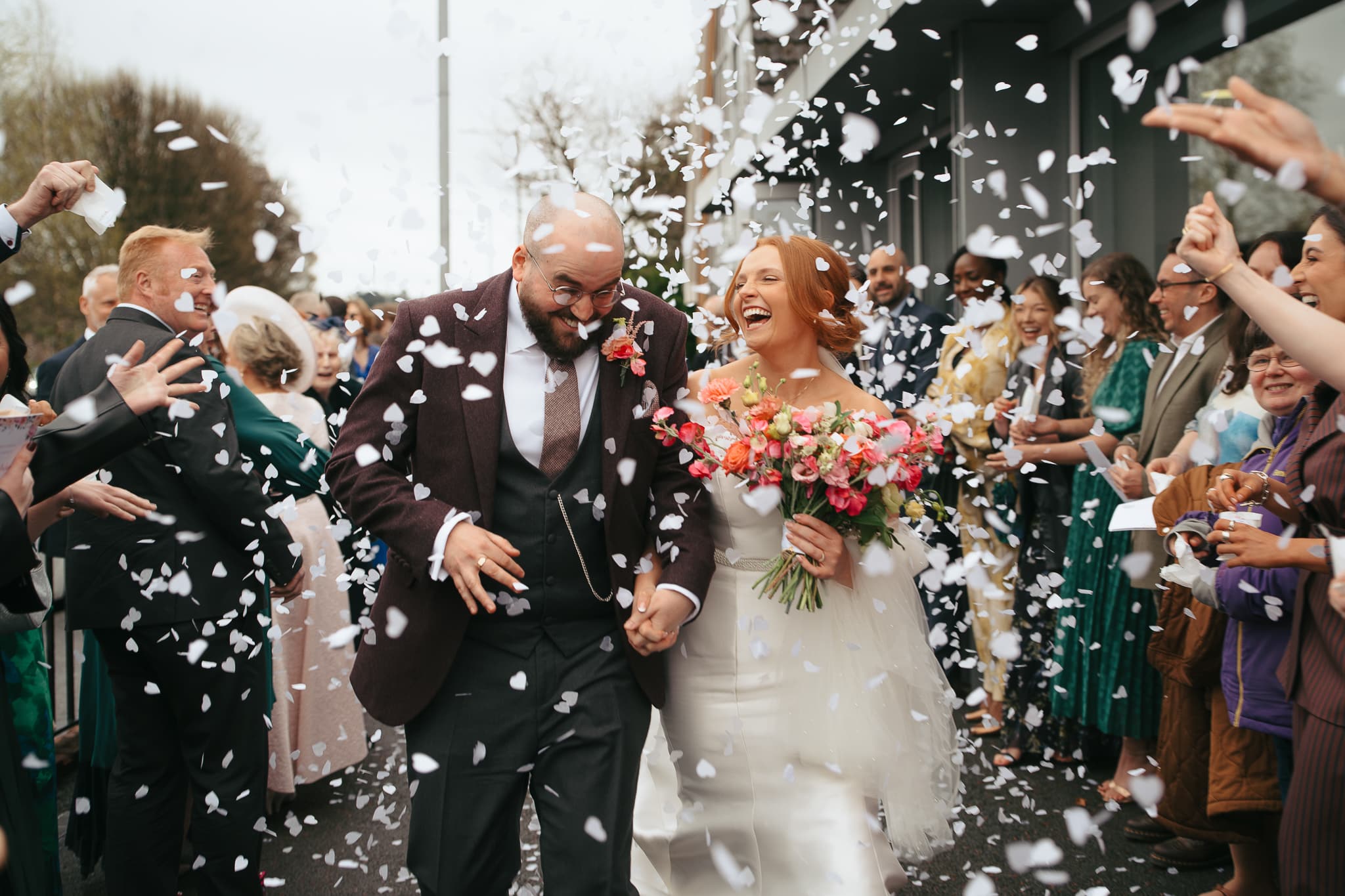 Bride and groom walking through confetti with guests cheering.