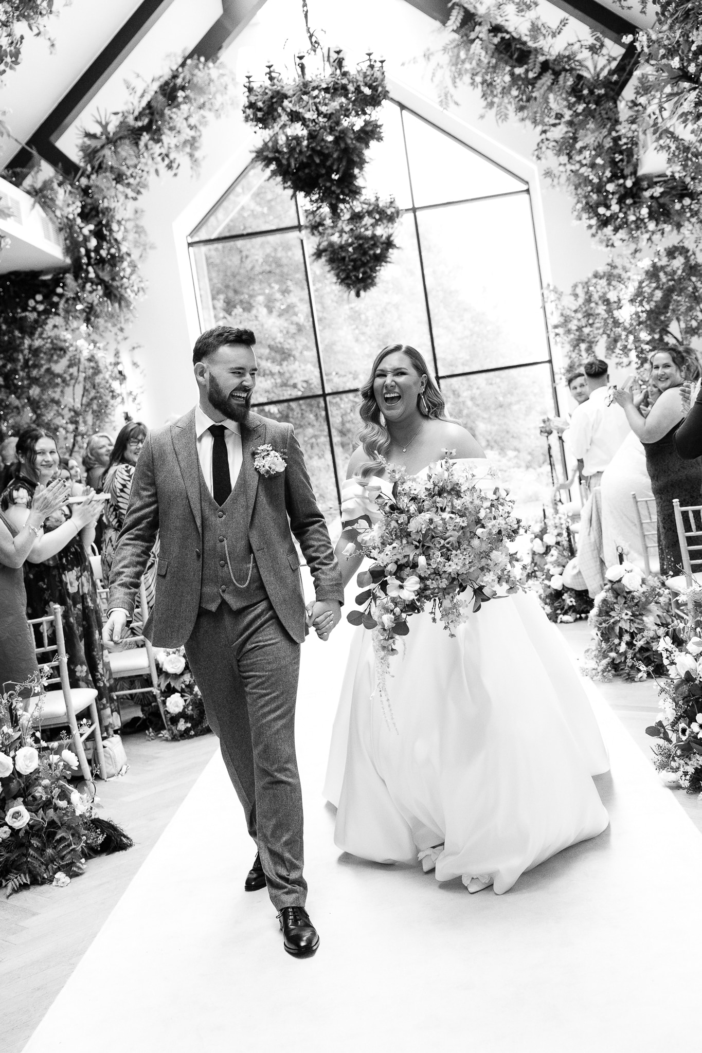Bride and groom joyfully walk down the aisle in a flower-adorned wedding venue.