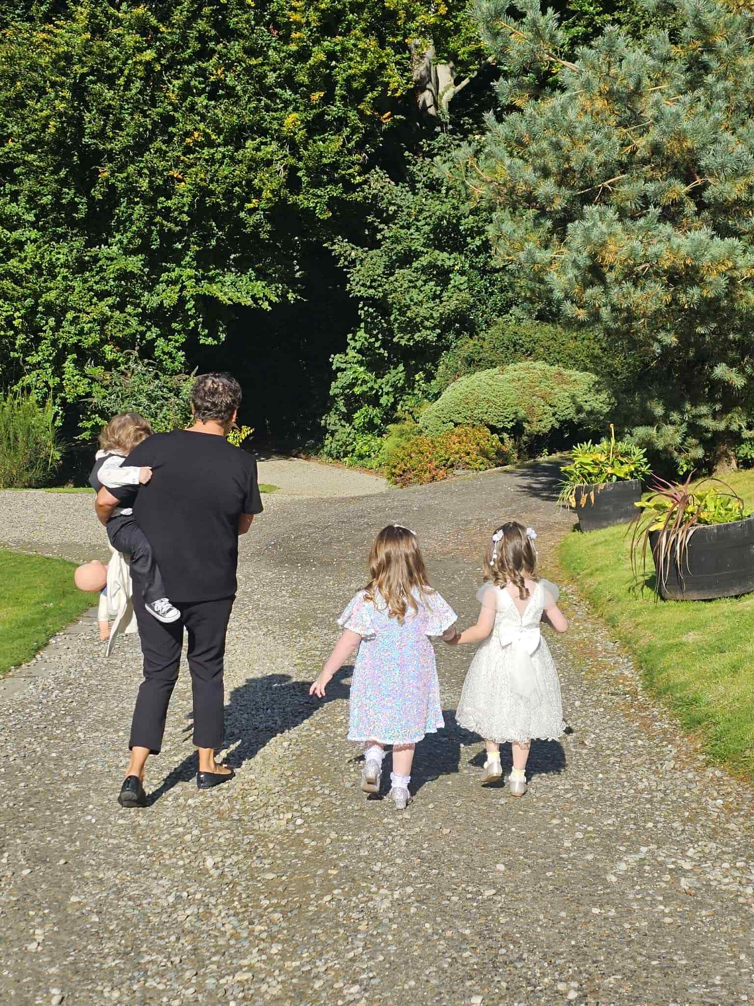 Adult and three children walking on a gravel path in a garden.
