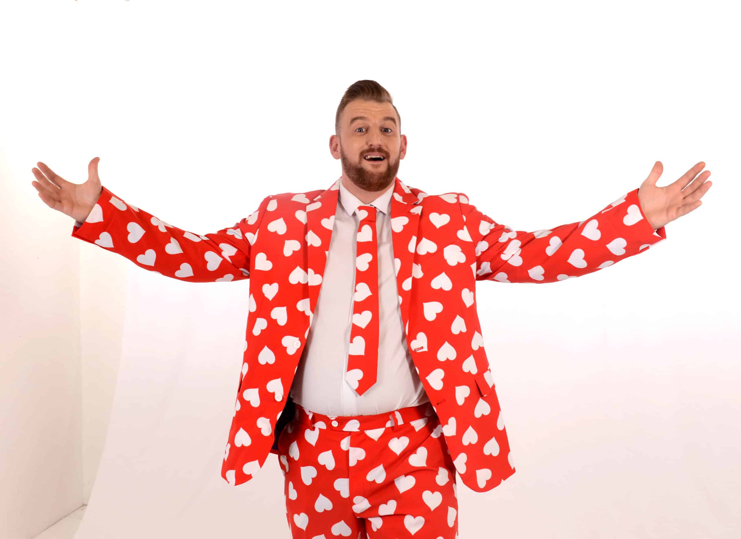 Man wearing a red suit with white heart patterns, arms outstretched, against a white background.