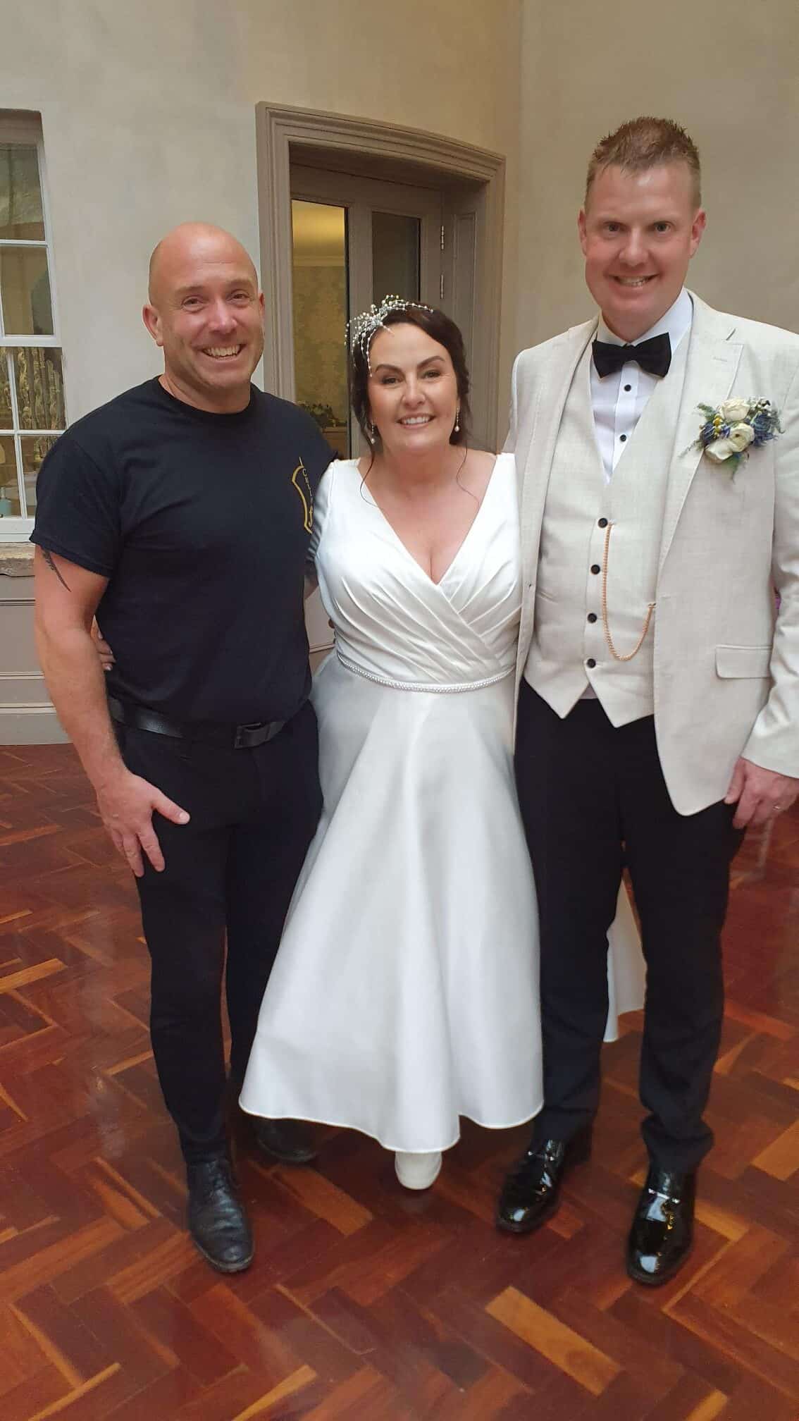 Bride in white dress with groom in suit and another man posing indoors.