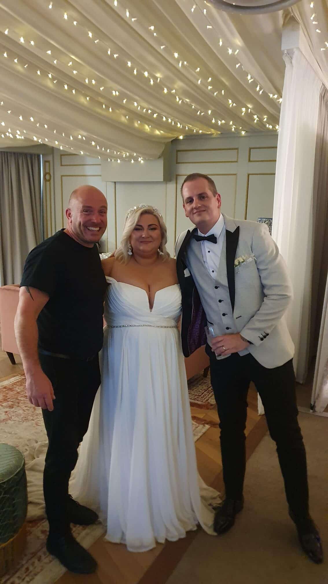Three people posing together at a wedding, with the bride in a white dress and two men in suits.