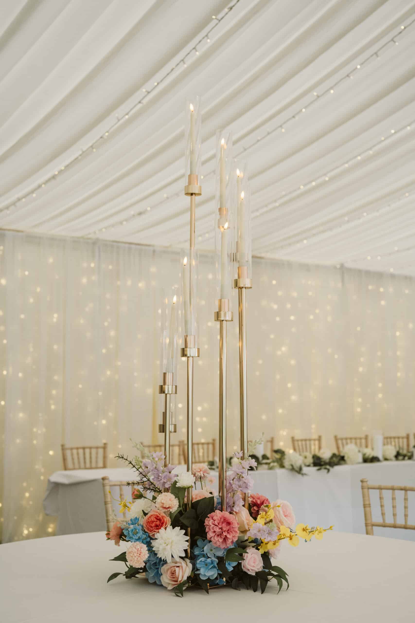 Elegant floral centerpiece with tall candles in a softly lit banquet setting.
