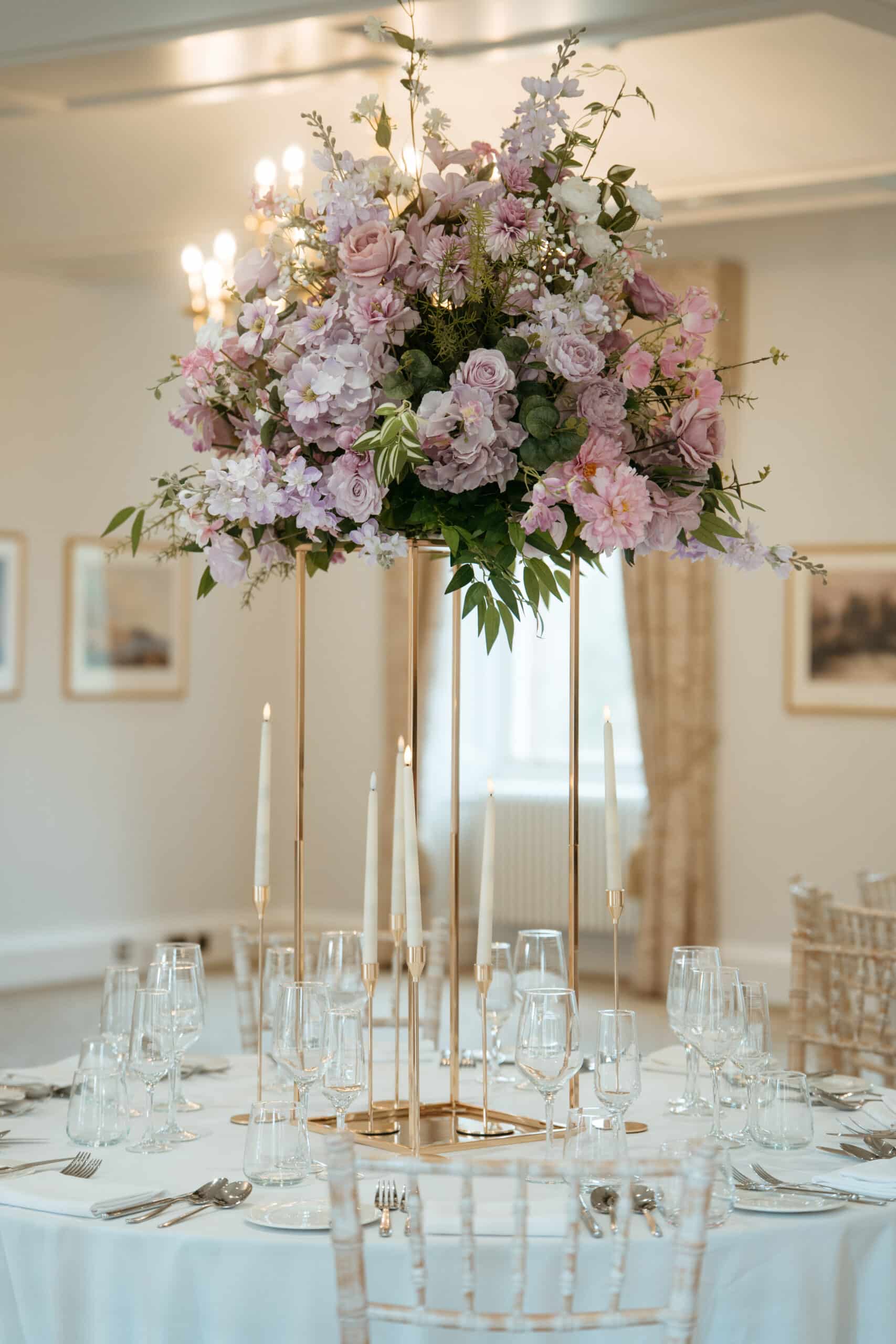 Elegant table setting with tall floral centerpiece and candles in a banquet hall.
