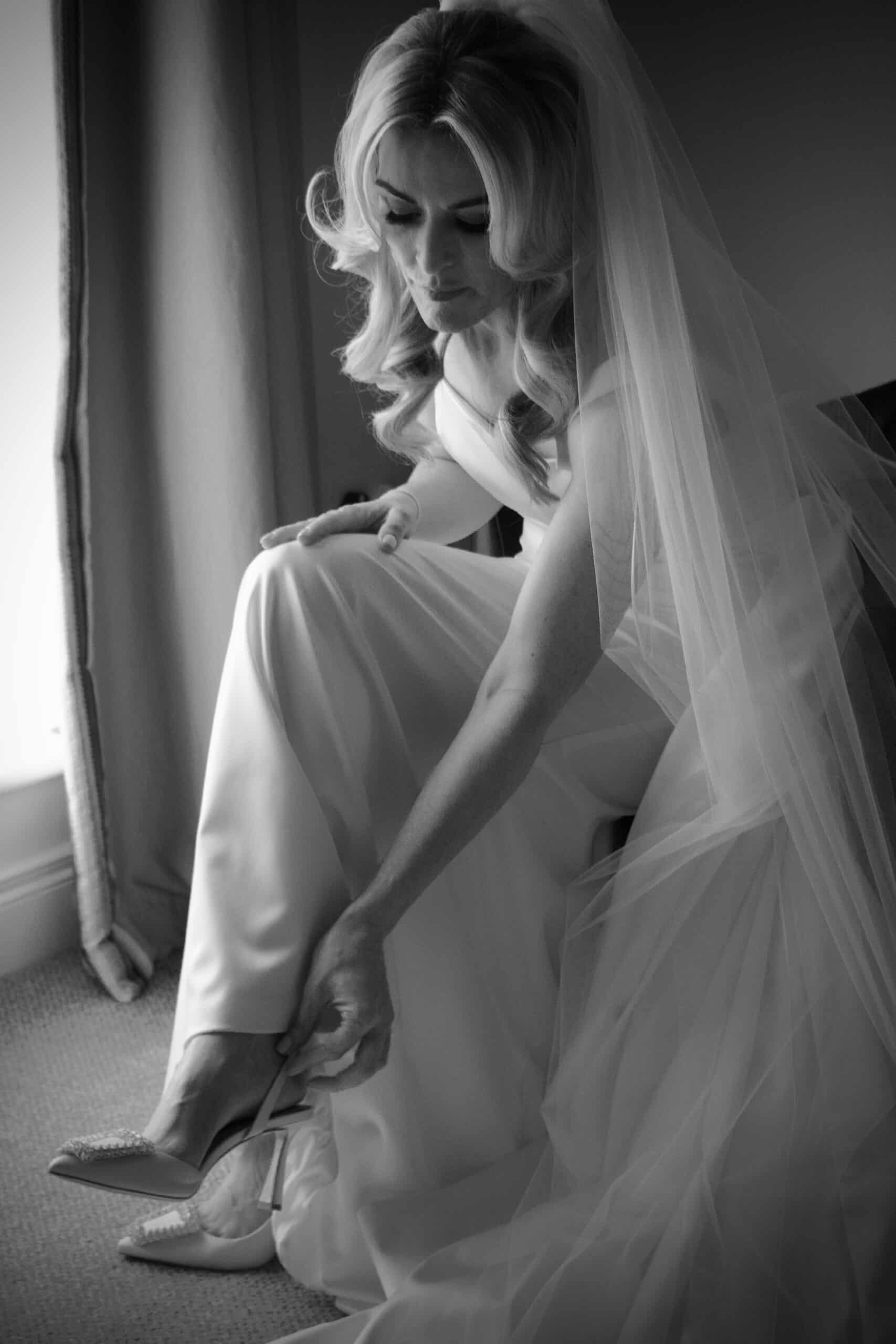 Bride in elegant gown adjusting her shoe, captured in a soft, contemplative moment.