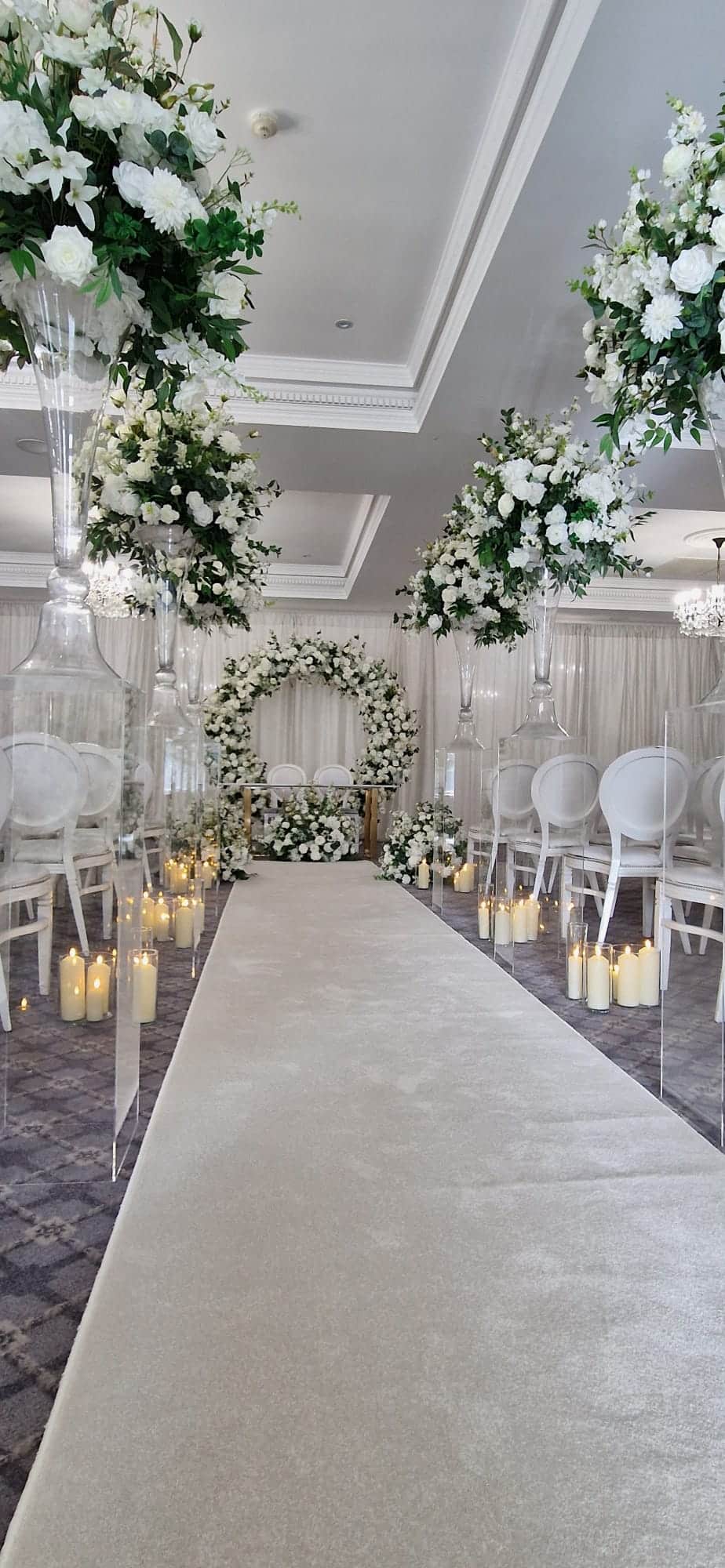 Elegant floral wedding aisle with white flowers, candles, and clear vases.