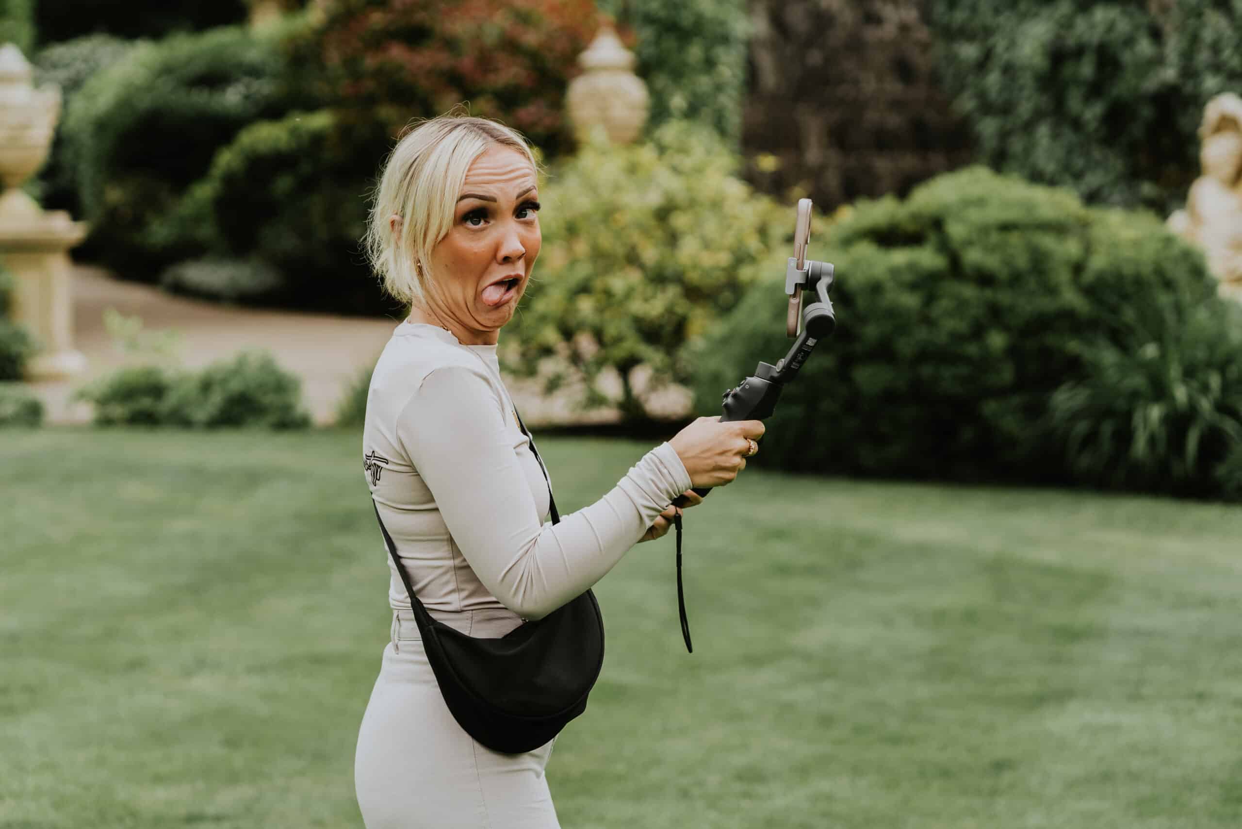 Person making a funny face while holding a phone on a gimbal in a garden setting.