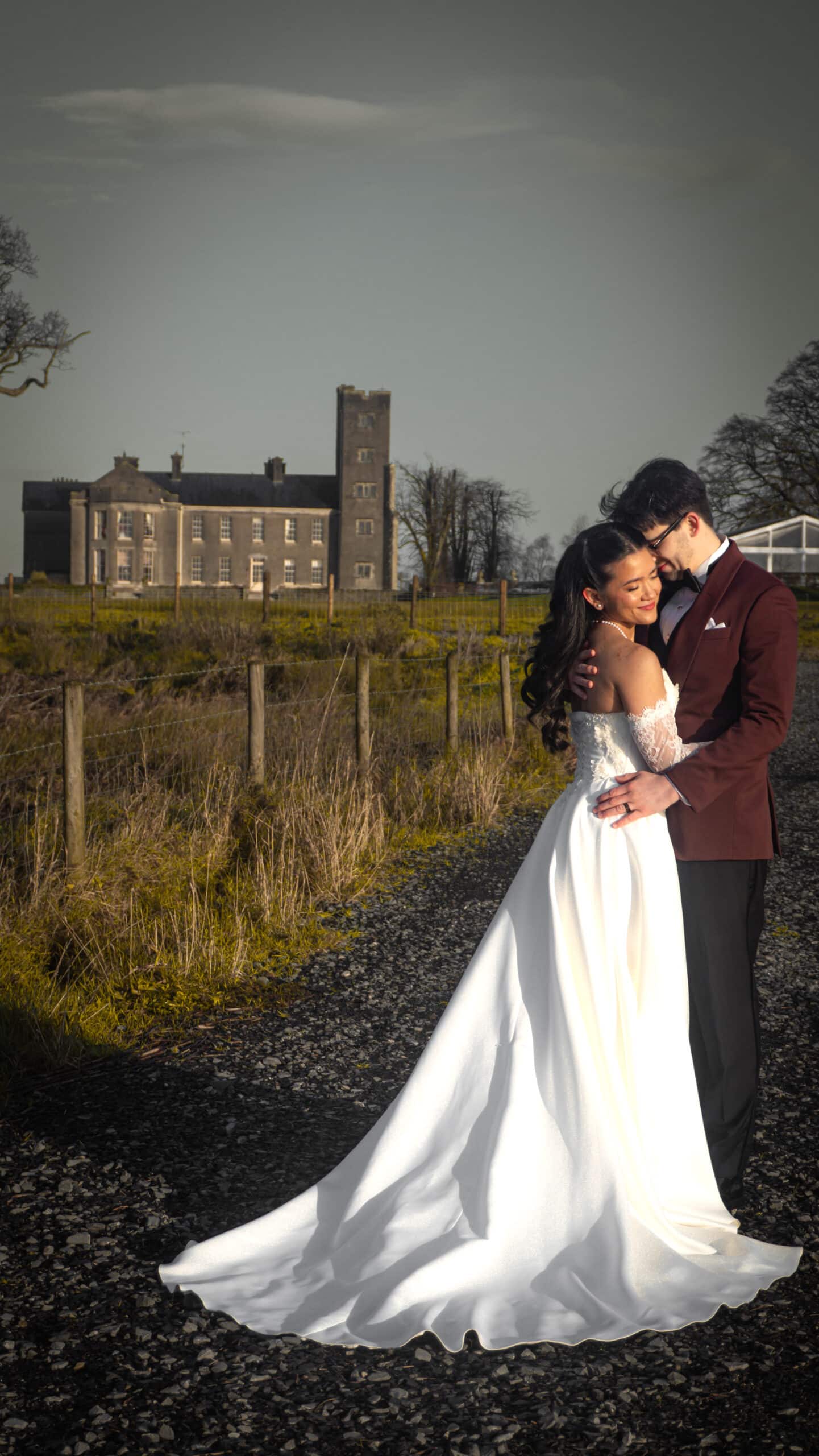 Bride and groom embrace outdoors with a historic building in the background.