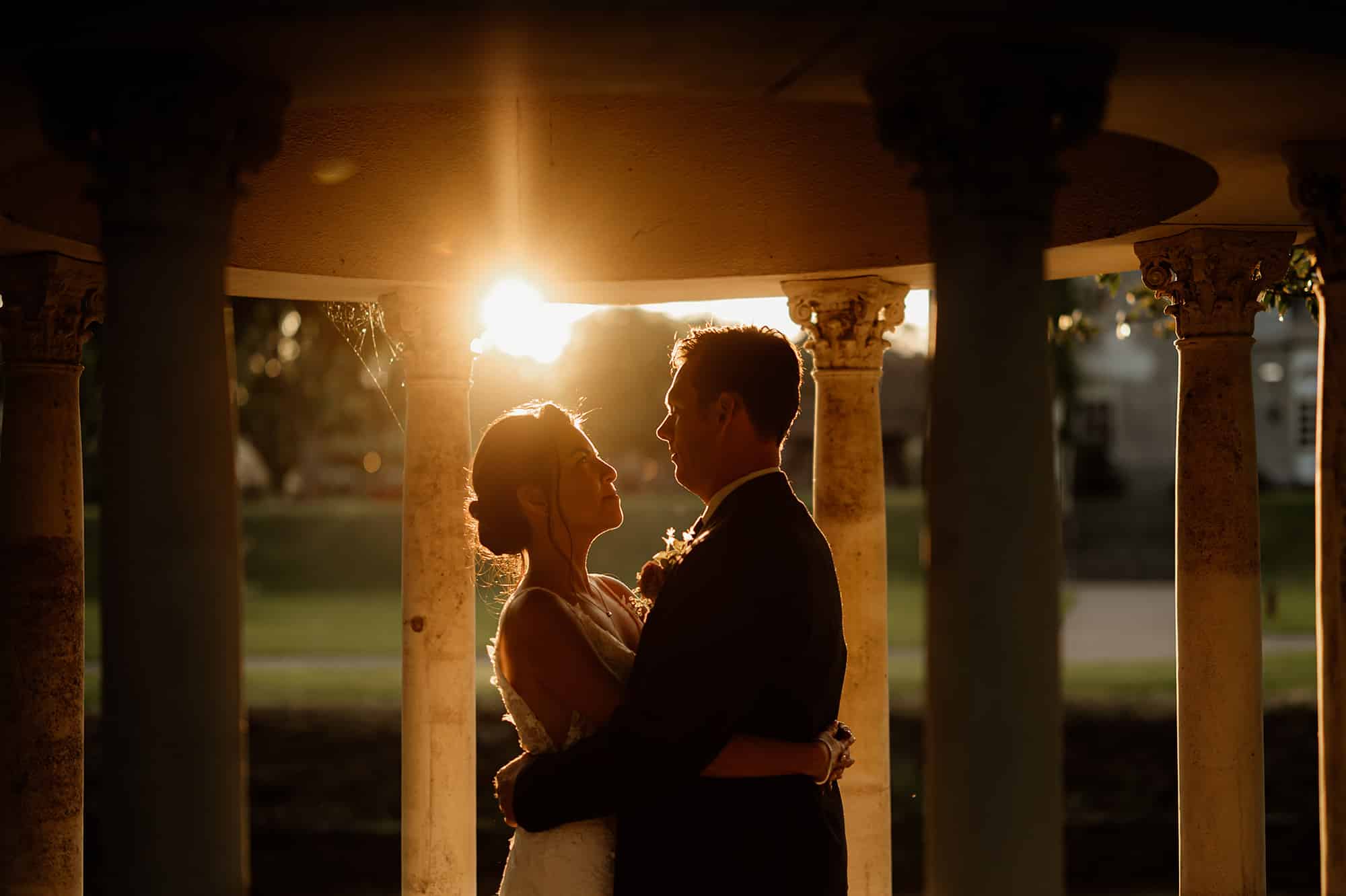 Couple embracing under columns at sunset.