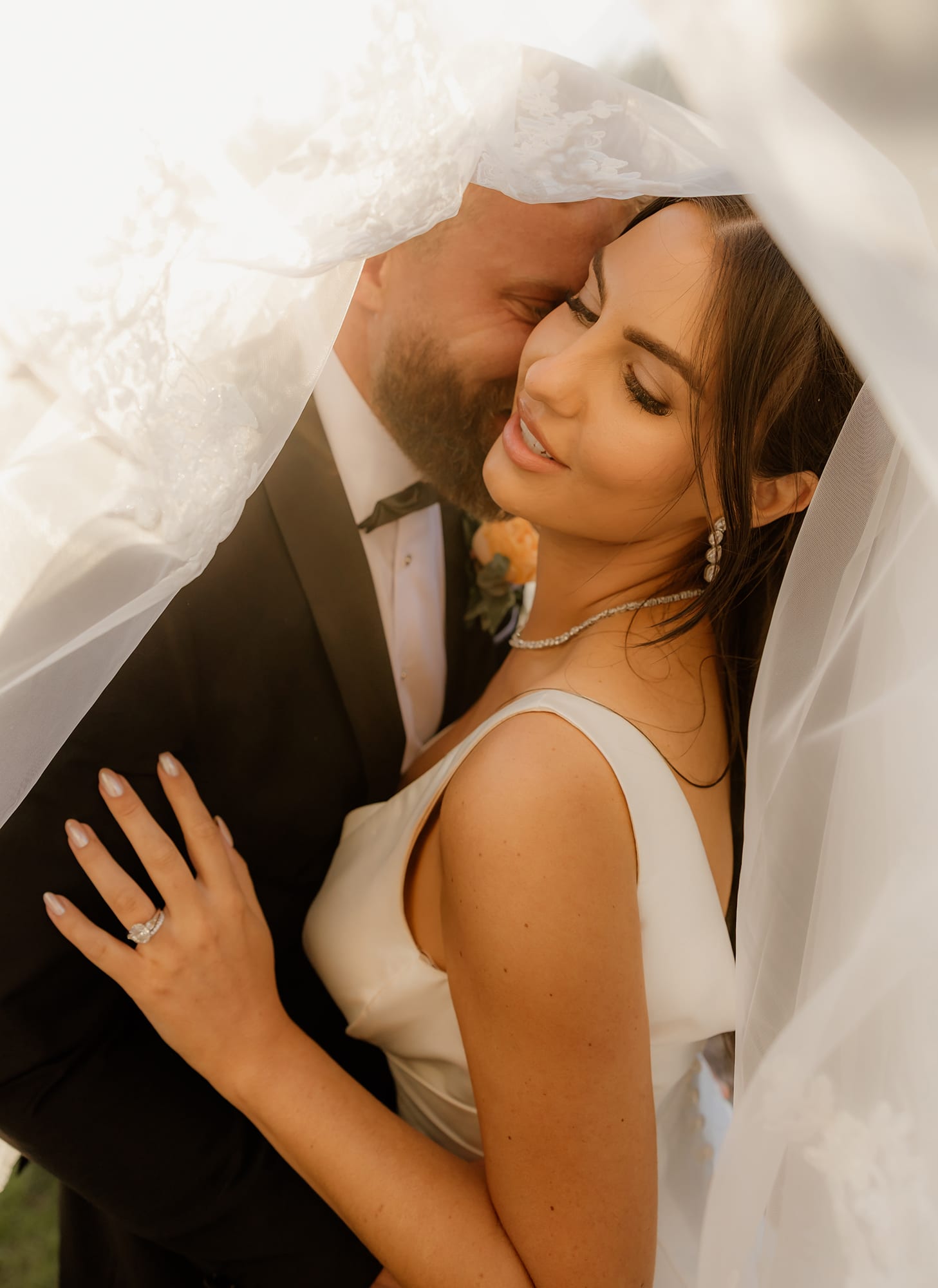 Bride and groom embrace under a veil, sharing a tender moment.
