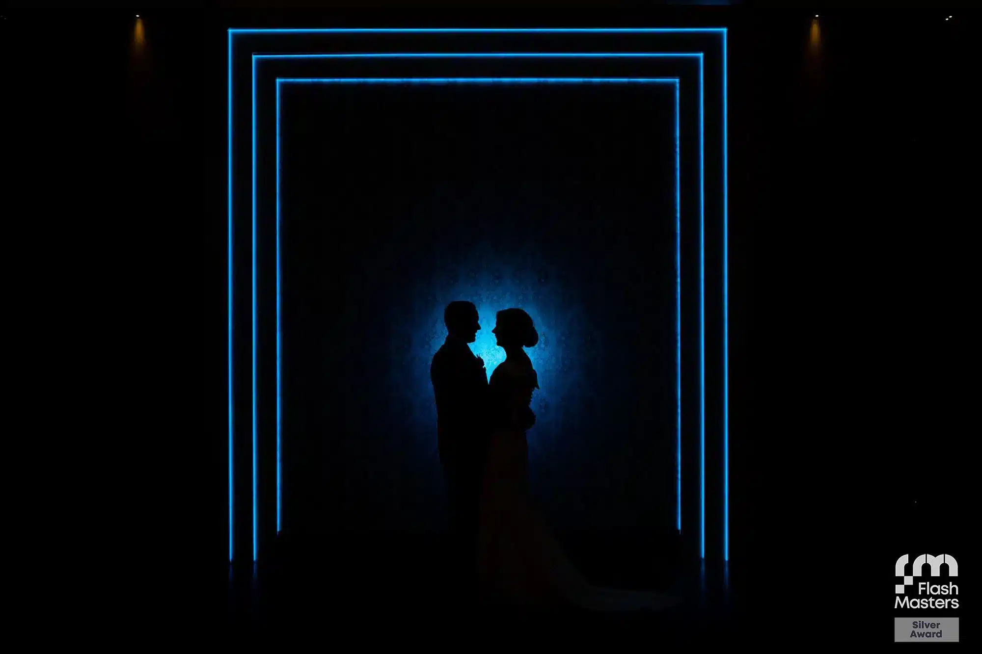 Silhouette of a couple in front of a blue neon-lit backdrop.