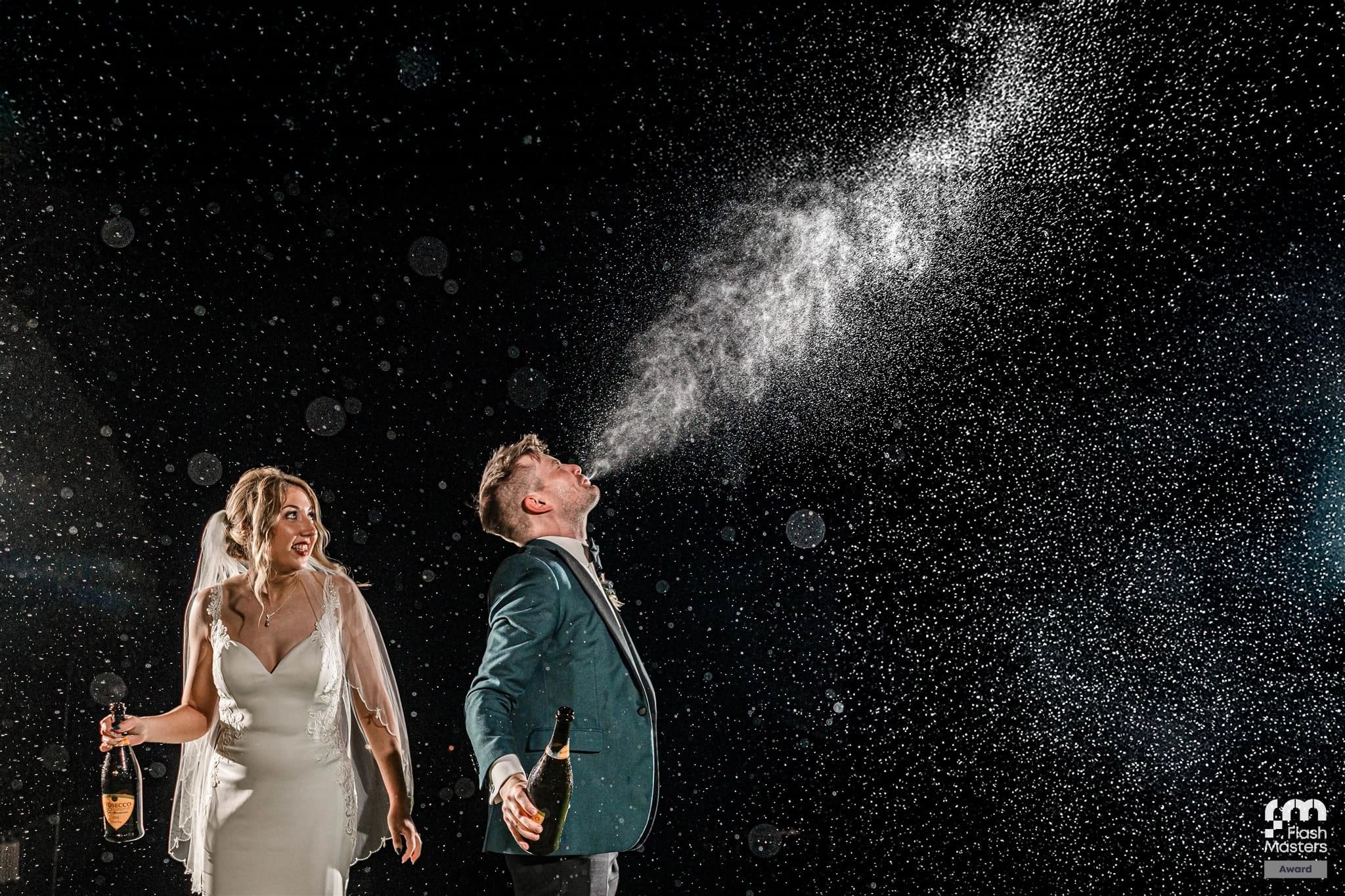 Bride and groom celebrate with champagne spray under starry night sky.