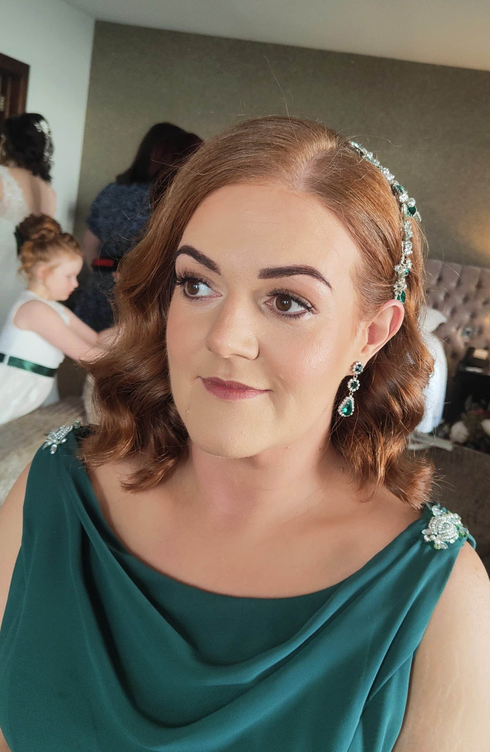 Woman in a green dress with matching jeweled accessories, focused expression, indoor setting.