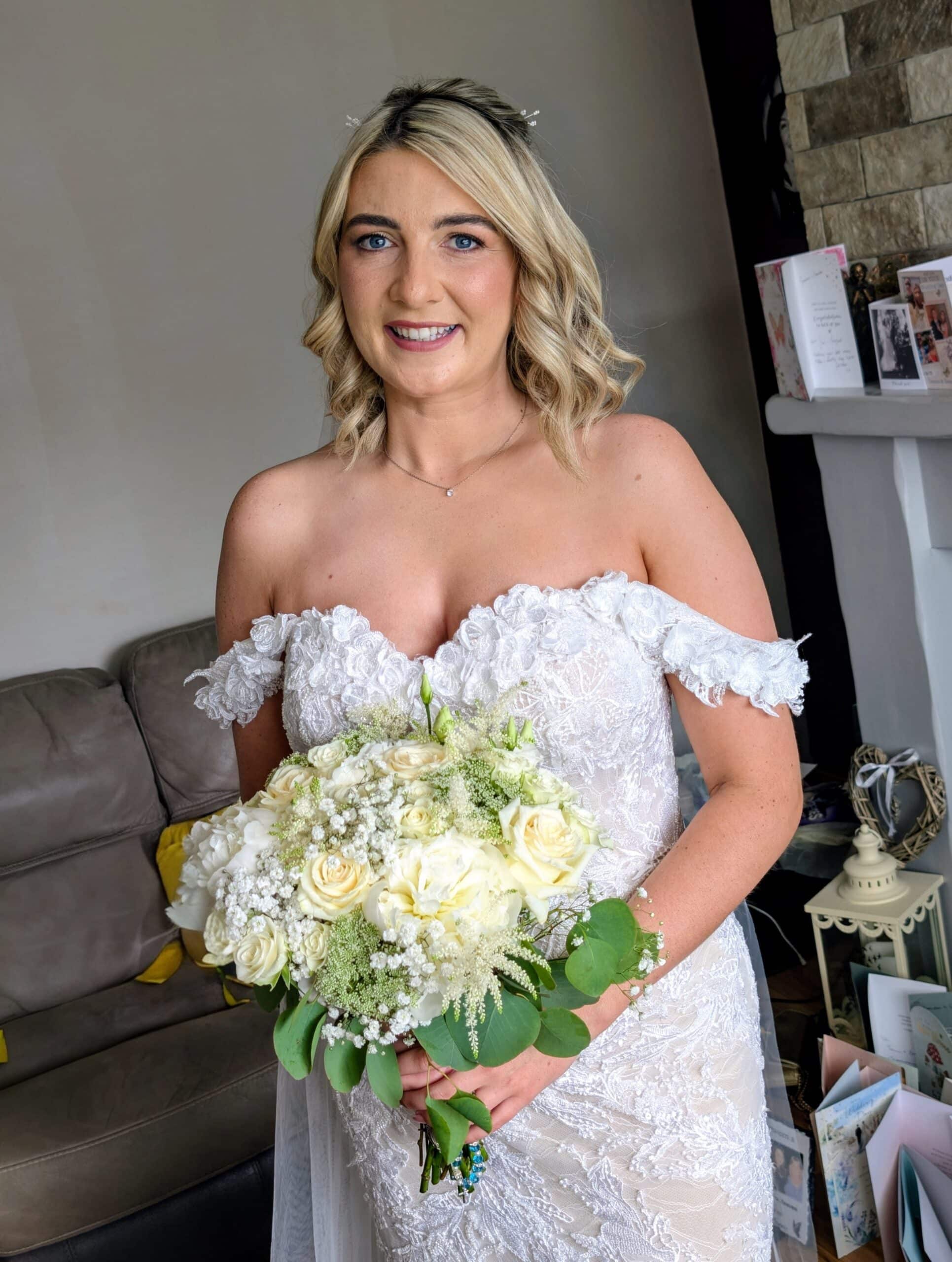 Bride in a lace wedding dress holding a bouquet of white flowers indoors.