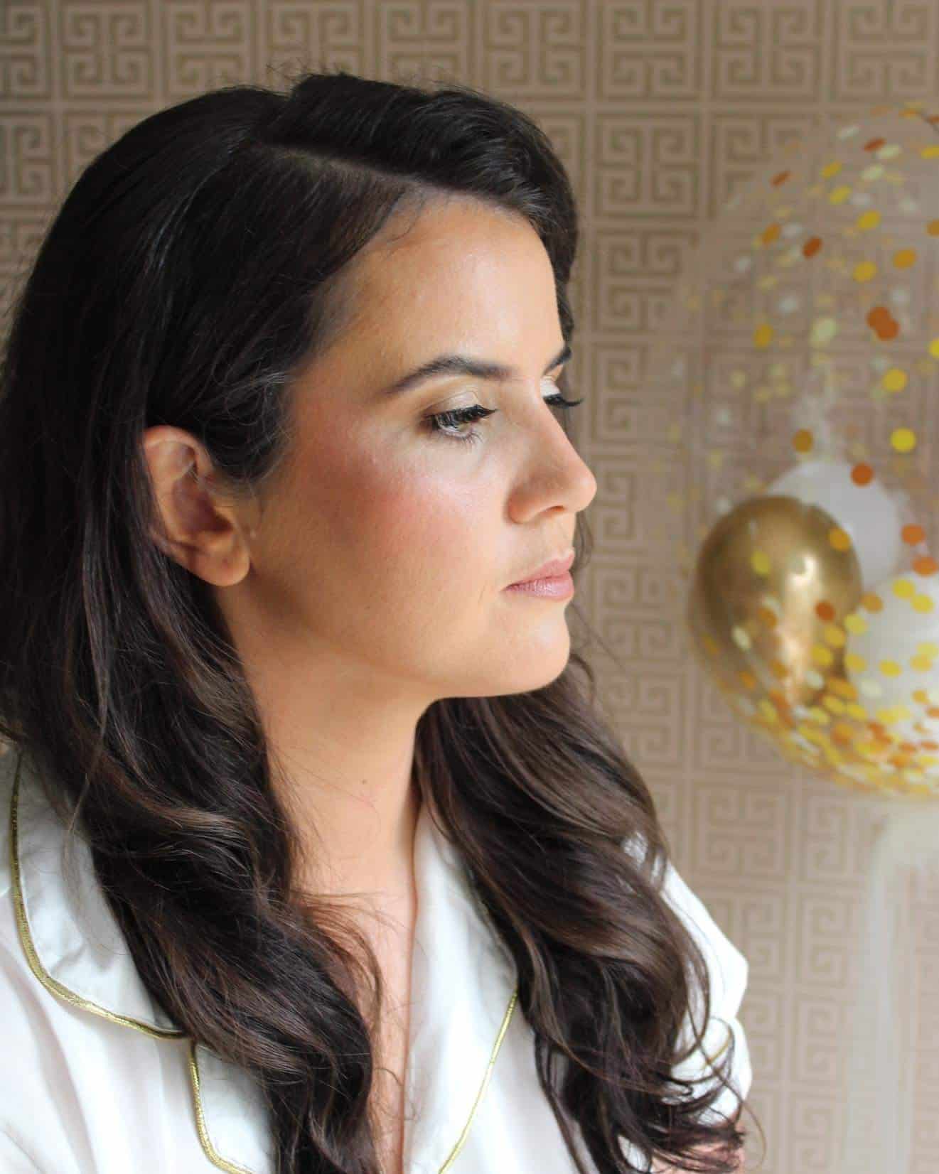 Woman with long dark hair in profile wearing a white blouse, ornate wallpaper and gold-accented balloon in background.