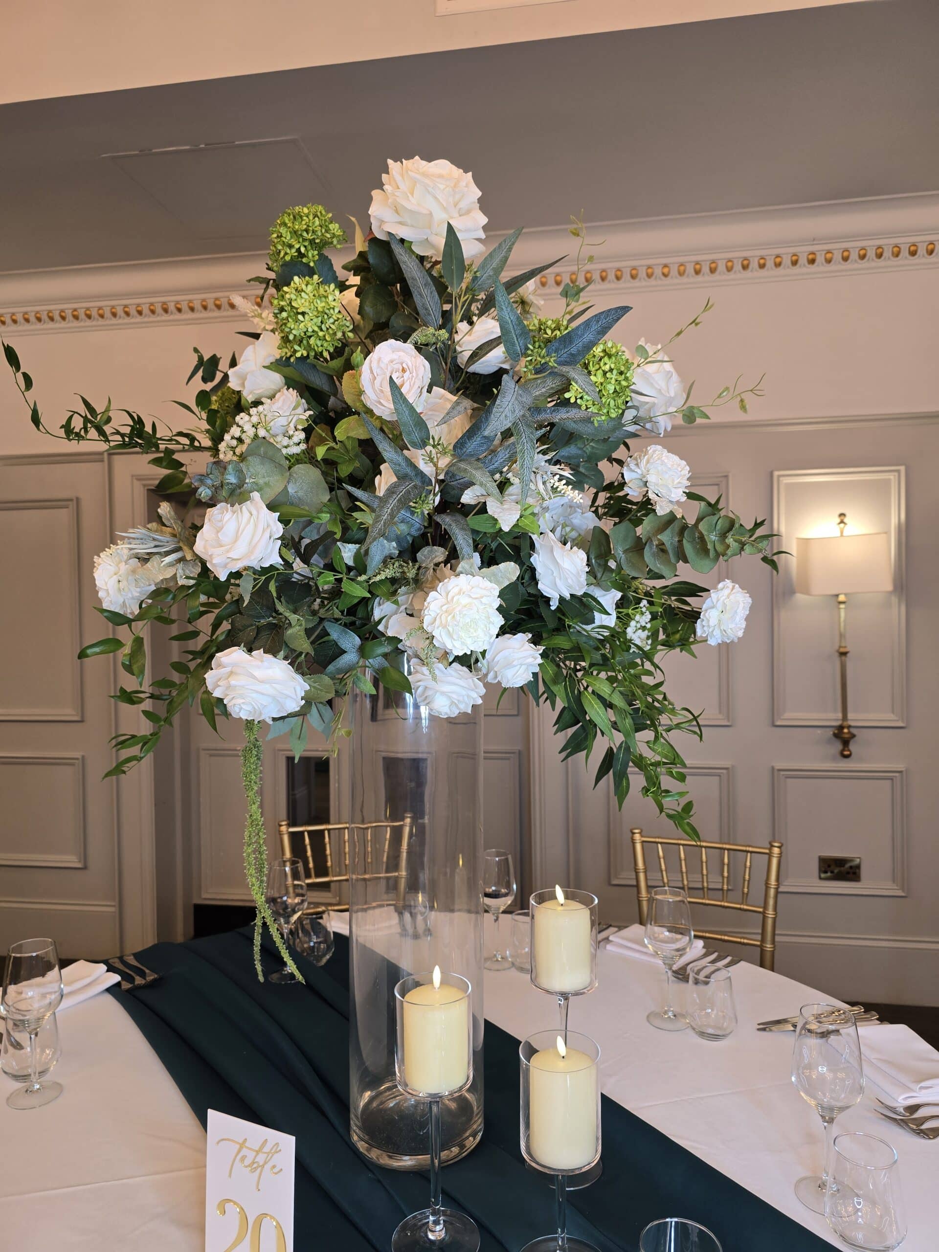 Elegant floral centerpiece with white flowers and greenery, surrounded by candles on a dining table, labeled "Table 20."