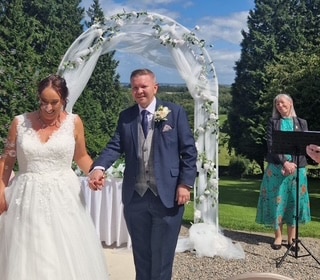 Bride and groom under a floral arch at an outdoor wedding ceremony.