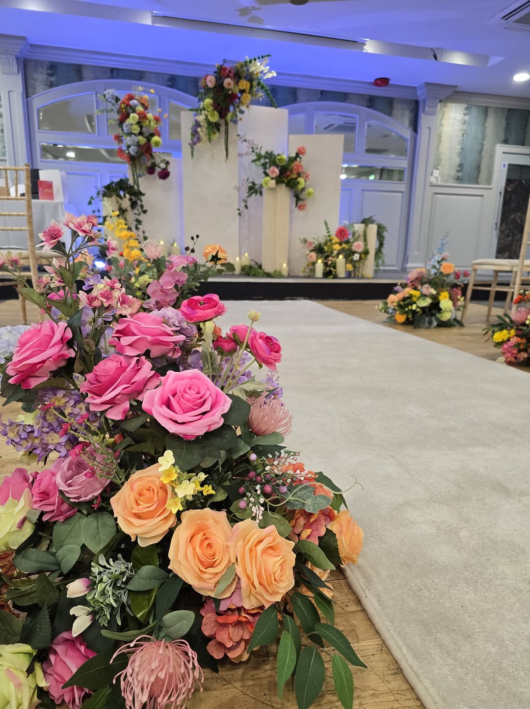 Flower arrangement with pink, orange, and purple blooms near a wedding altar under blue lighting.