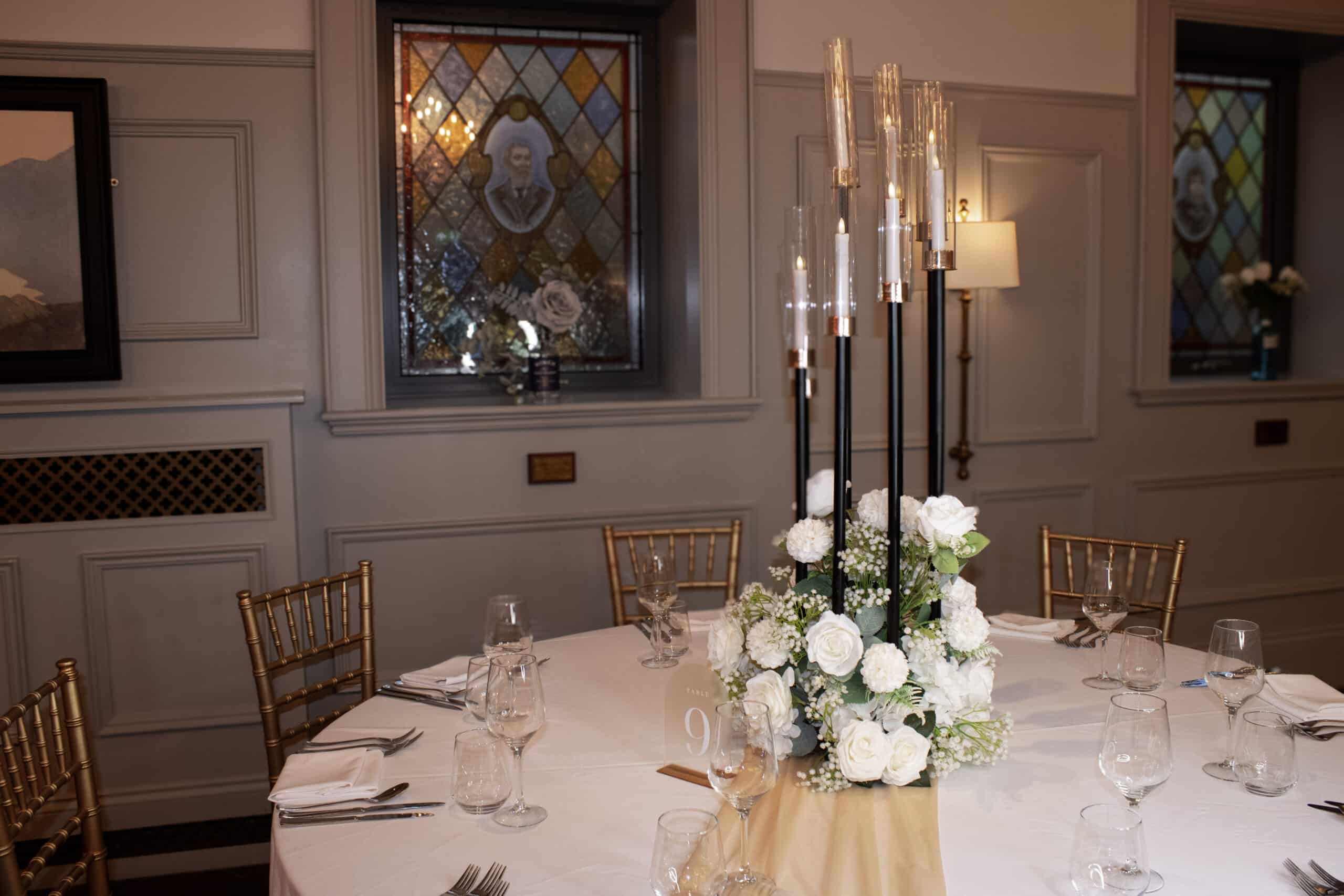 Elegant table setting with floral centerpiece and tall candles in a room with stained glass windows.