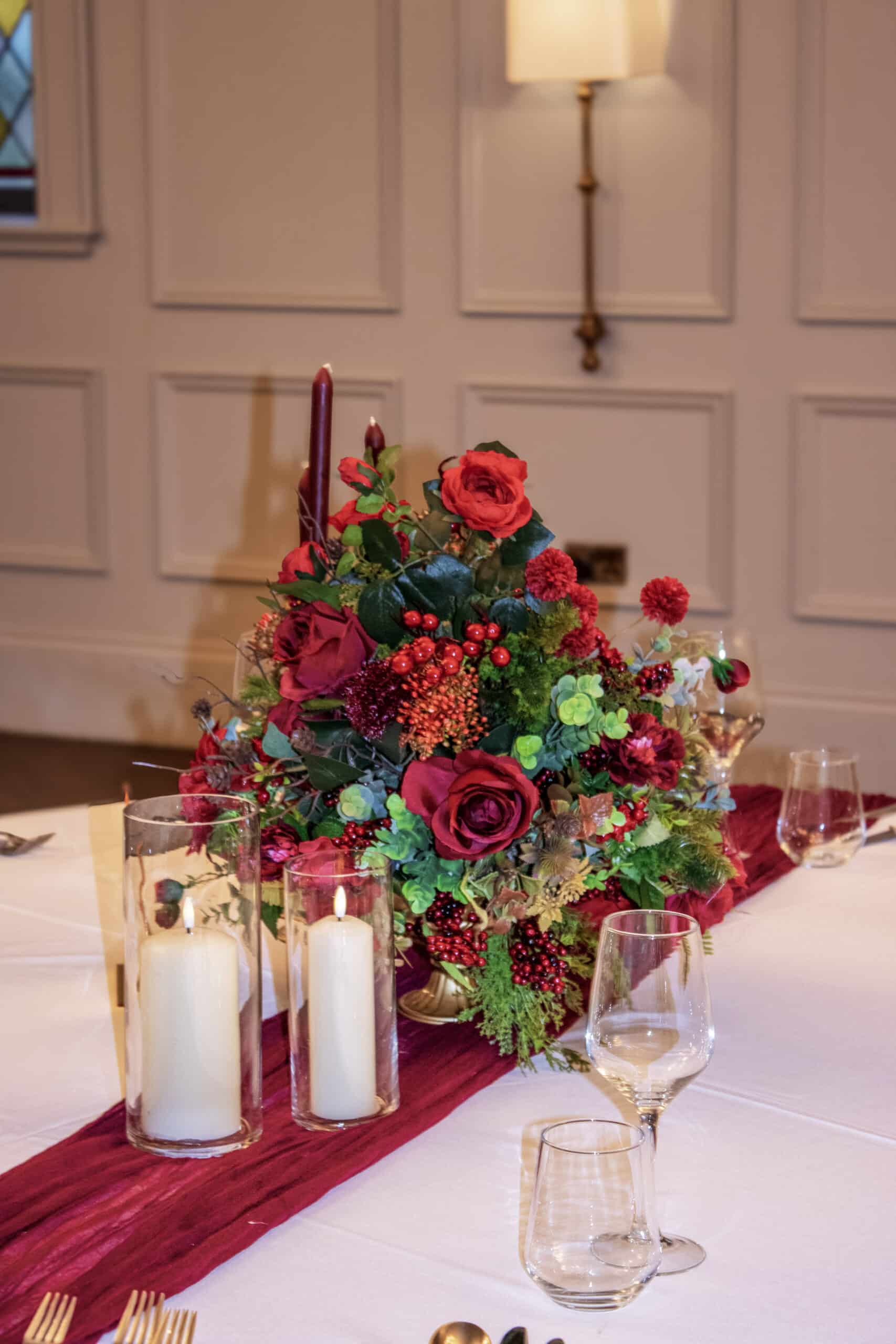 Elegant floral centerpiece with red roses and candles on a table.