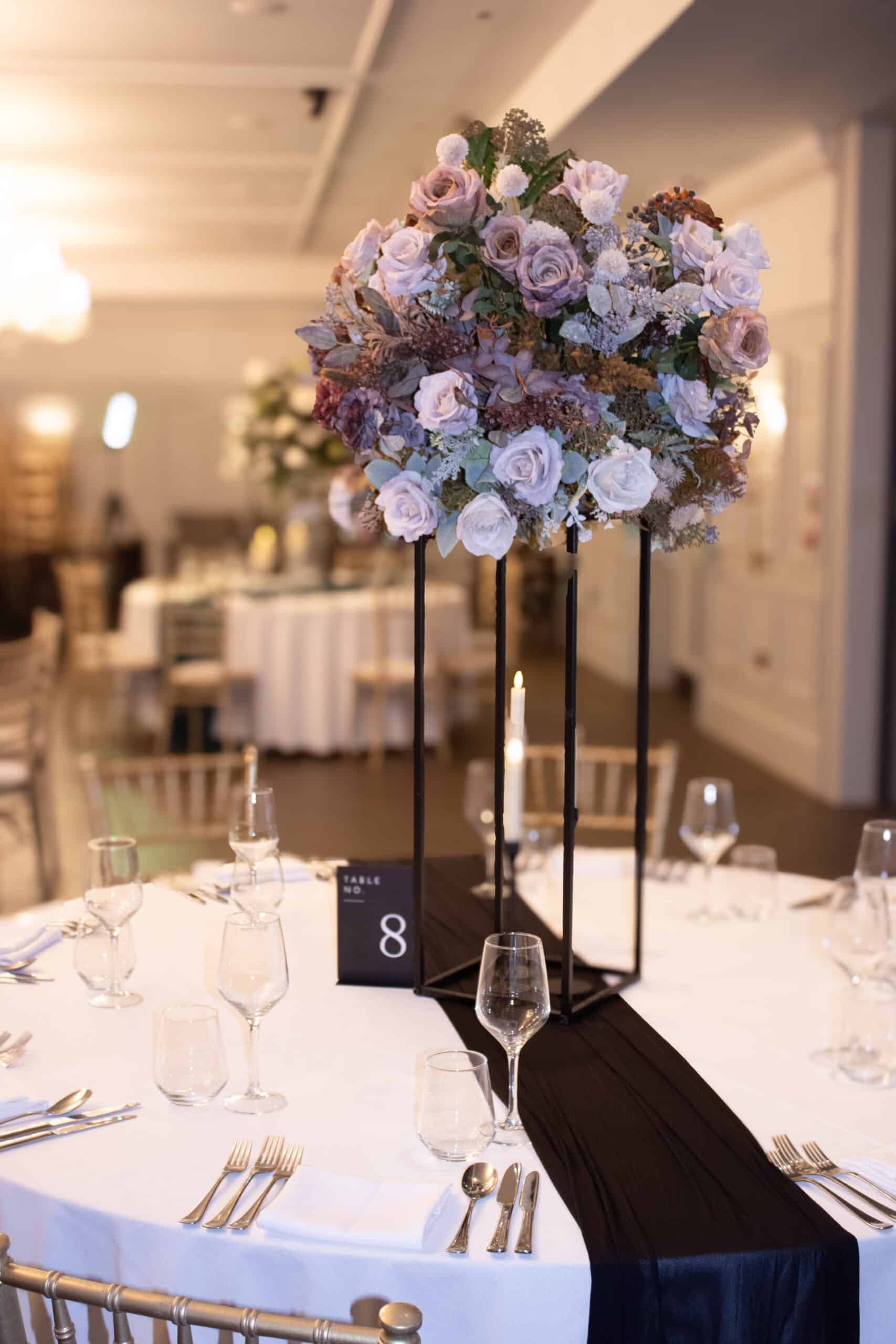 Elegant wedding table setting with floral centerpiece, black table runner, and table number eight.