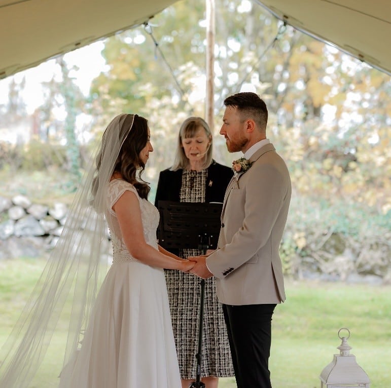 Bride and groom holding hands during outdoor wedding ceremony with officiant.